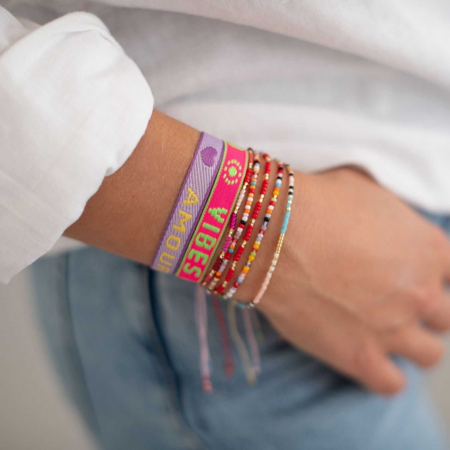 Statement Armband - neon Love, Amour lila mit Glasperlen am Arm einer Frau. Größenverstellbar, wasserfest, ideal als Geschenk oder modisches Accessoire.