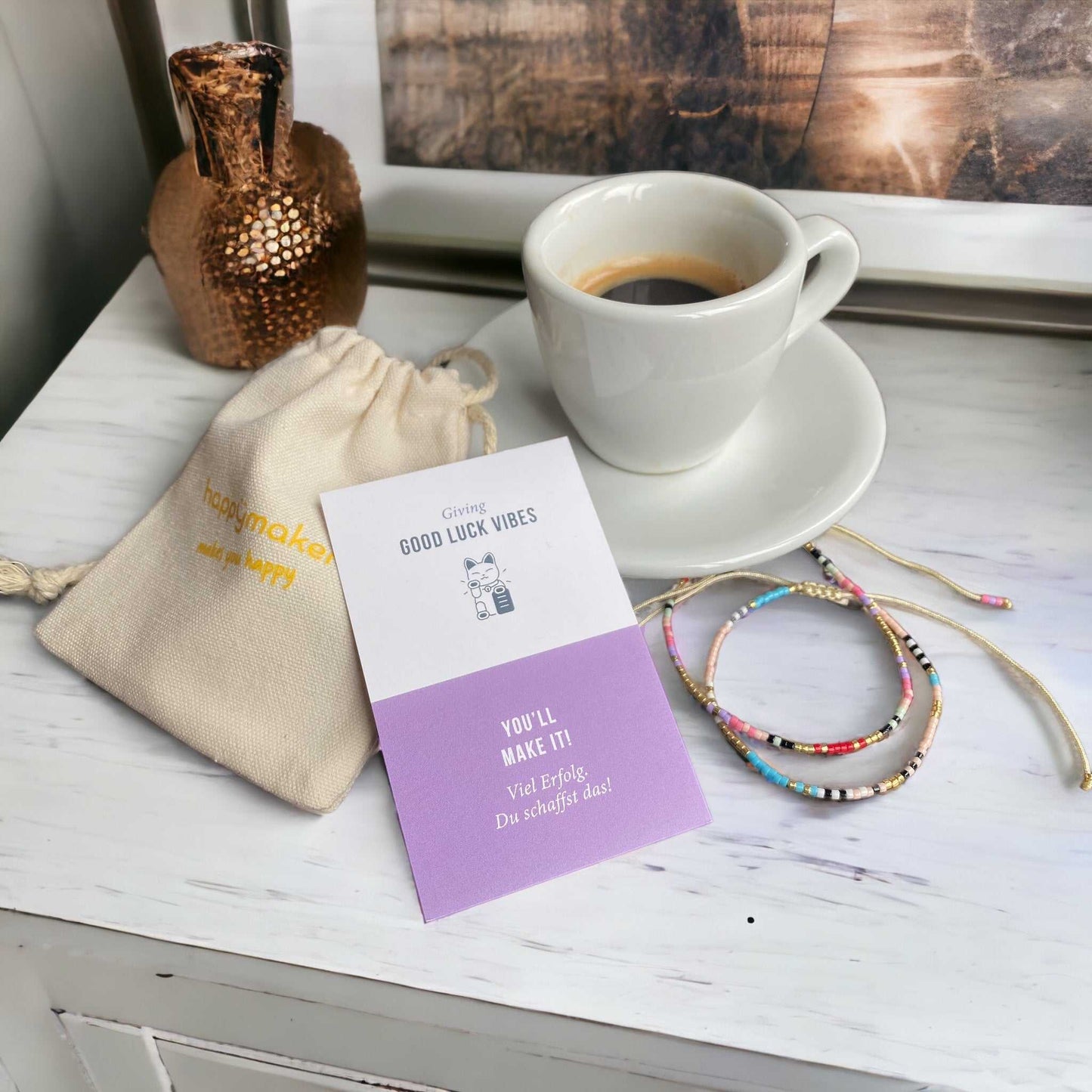 Freundschaftsarmband mit bunten Glasperlen, einzeln verpackt in Baumwollsäckchen auf Tisch neben Kaffeetasse.