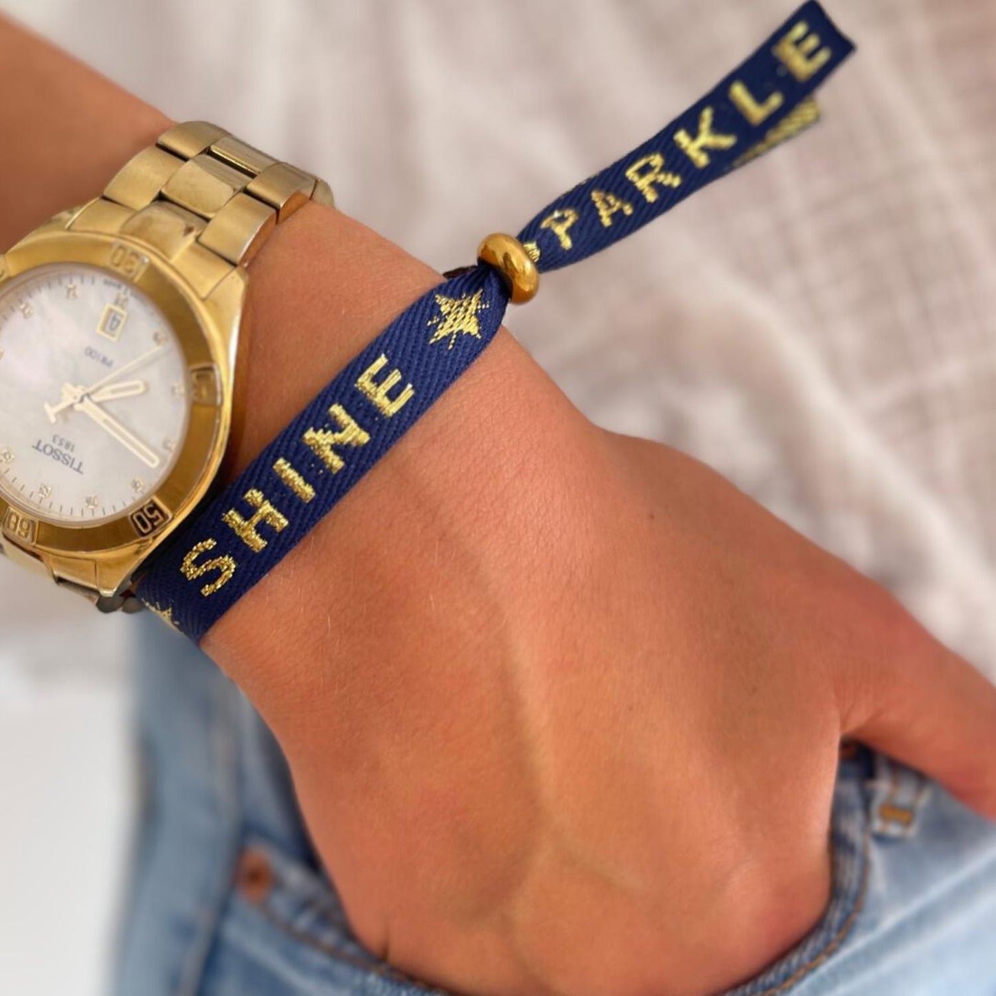 Statement-Armband mit goldener Aufschrift „SHINE SPARKLE“, das mit verstellbarer Perle und wasserdichtem Stoff am Handgelenk getragen wird.
