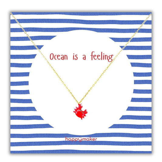 Gold Kette mit Anhänger auf gestreifter Karte mit "Ocean is a feeling" Schriftzug.