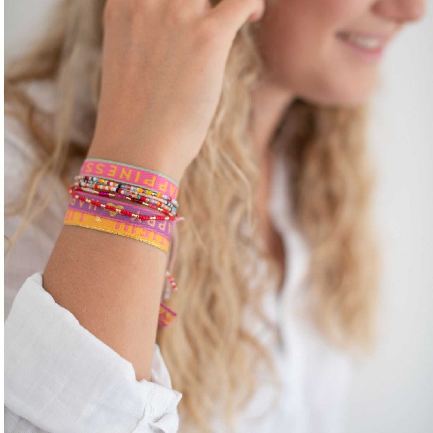 Boho Armbänder Set mit rosa „Happiness“ und lila „Happy“ Armbändern und bunten Glasperlen am Arm..