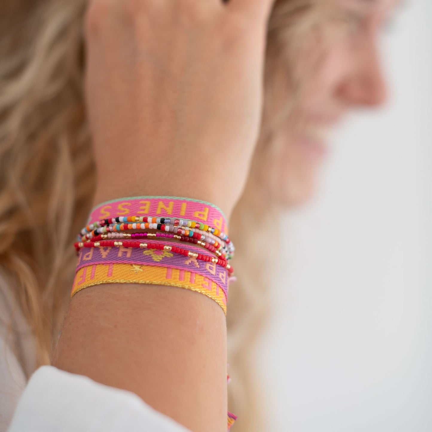 stoffarmbänder mit happiness, live is beautiful und happiness und perlenarmbänder am arm einer frau