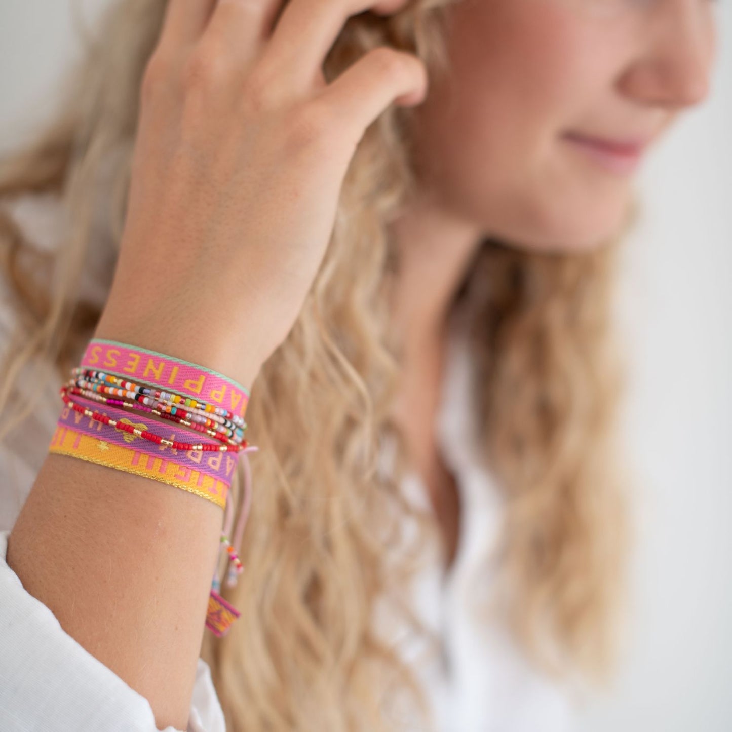 stoffarmbänder mit happyness, life is beautiful und happy und perlenarmbänder am arm einer blonden frau