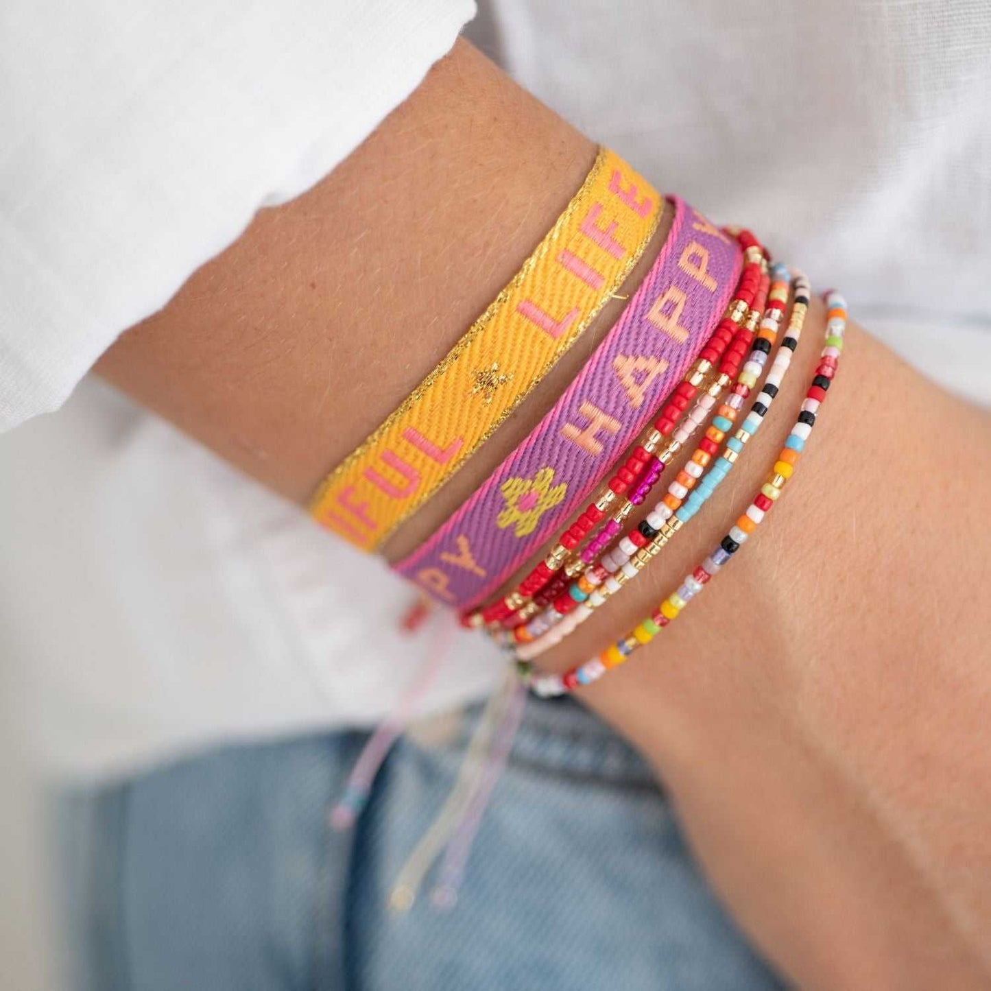Statement Armband in gelb und lila mit Perlenarmbänder am Arm getragen.