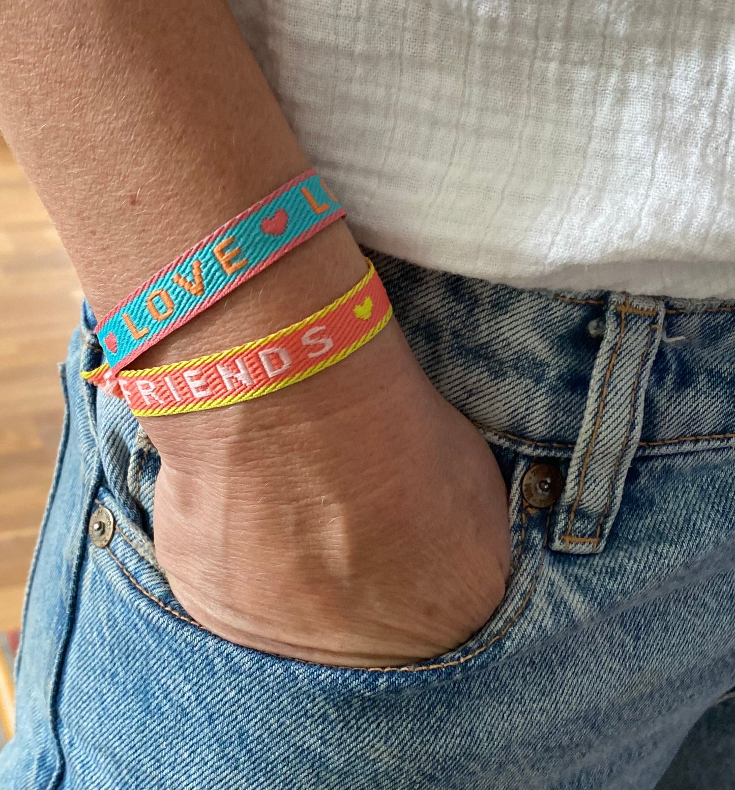 stoffarmband in grün mit Live und eines in orange mit Friends gewebt am arm einer frau