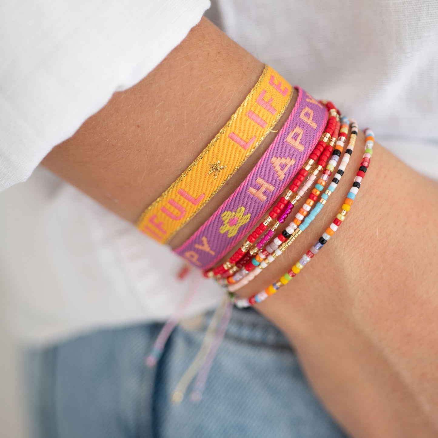 stoffarmbänder mit happy und life is beautiful gewebt und perlenarmbänder am arm einer frau 