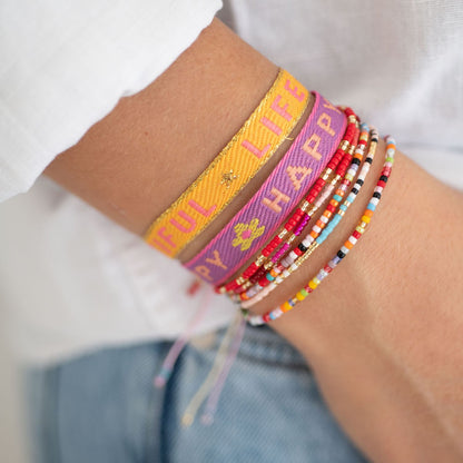 stoffarmbänder mit happy und life is beautiful gewebt und perlenarmbänder am arm einer frau 