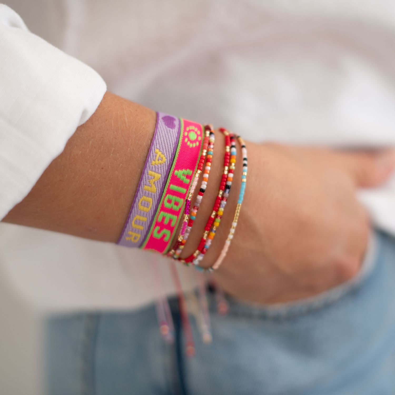 stoffarmband in neon pink mit good vibes und lila mit amour gewebt. mit perlenarmbändern am arm einer frau